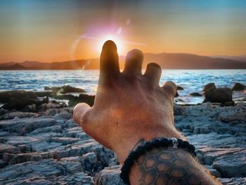 Close-up of hand against sea during sunset