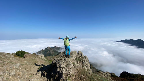 Rear view of man standing on mountain against clear blue sky