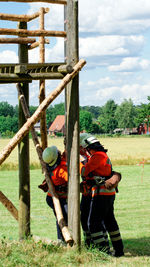 Firefighters standing by built structure over grass field against sky