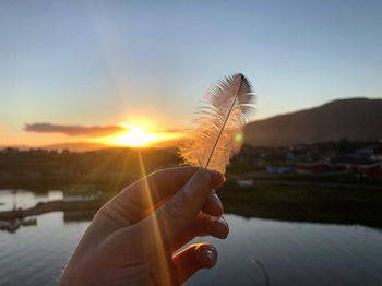 Close-up of hand holding sun against sky during sunset