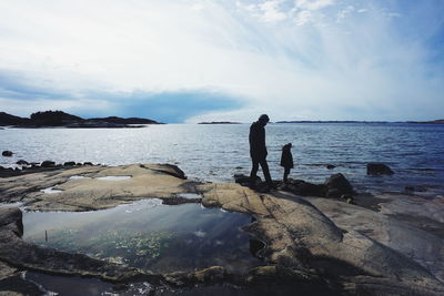 Man and child walking on rocks by sea against sky