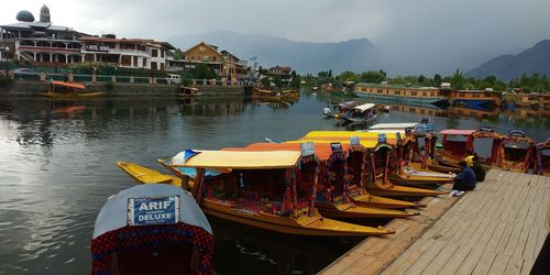 Boats moored in river by buildings against sky