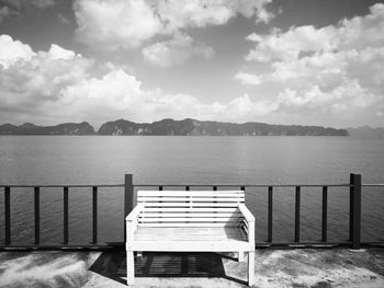 Empty bench by lake against sky