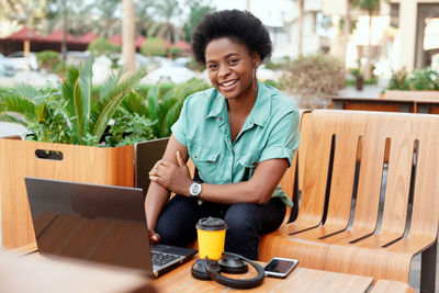 Portrait of smiling young woman using laptop on table at cafe