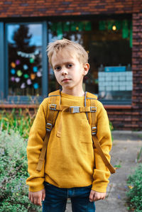 Tired boy in a yellow sweater with a yellow backpack in the schoolyard. back to school in september.