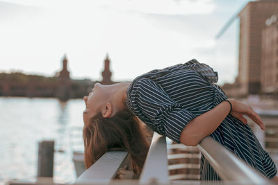 Side view of woman leaning on railing against sky