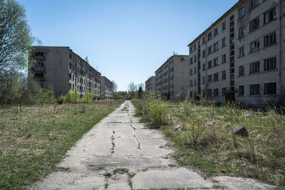 Surface level of road amidst abandoned buildings against clear sky