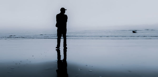 Silhouette man standing on beach against sky