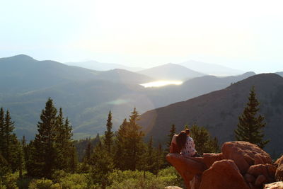 Woman sitting on mountain against sky