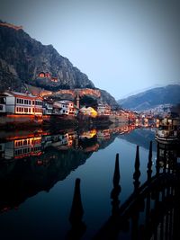 Buildings by river against clear sky at dusk