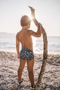 Full length of shirtless boy standing at beach against sky