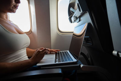 Midsection of woman using mobile phone while sitting in airplane