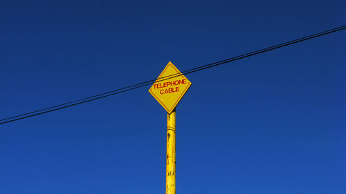 Low angle view of sign board by cable against clear blue sky