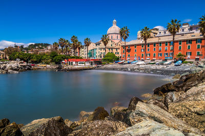 Buildings by river against clear blue sky