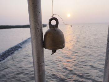 Electric lamp hanging on pole by sea against sky