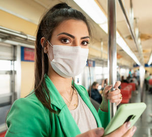 Portrait of young woman wearing mask listening music while standing in train