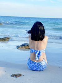 Rear view of woman at beach against sky