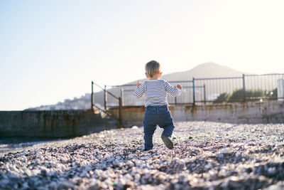 Rear view of boy standing on street against clear sky