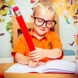 Boy writing in book with large pencil in school