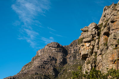 Low angle view of rocky mountain against blue sky