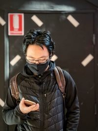 Portrait of young man holding camera while standing at home