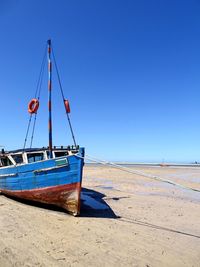 Boat moored on beach against clear blue sky