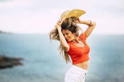 Young woman standing at beach against sky