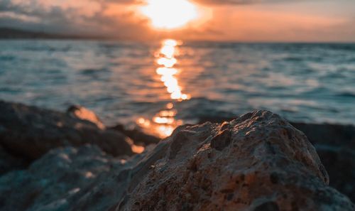 Close-up of rocks in sea against sunset sky