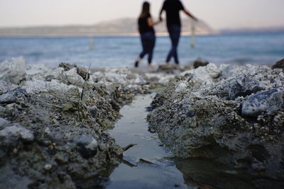 People standing on rocks at beach against sky