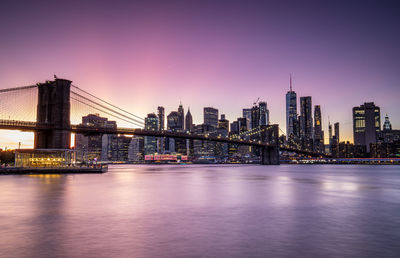 Illuminated bridge over river against buildings in city