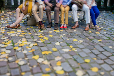 Low section of people sitting at footpath in city during autumn