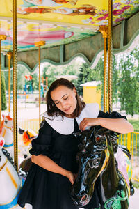 Beautiful brunette girl in a black dress poses on a bright carousel with horses