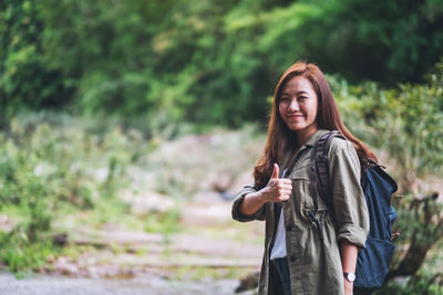 A female traveler with backpack making and showing thumbs up hand sign while walking in mountain