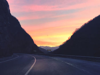 Road by mountains against sky during sunset