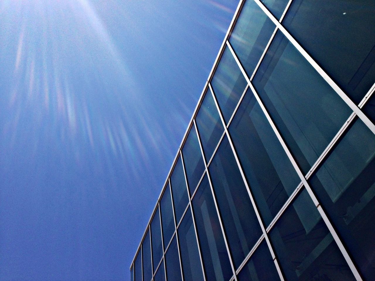 low angle view, modern, built structure, architecture, blue, building exterior, skyscraper, office building, sky, glass - material, tall - high, sunlight, clear sky, city, reflection, day, sunbeam, tower, no people, outdoors