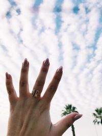 Close-up of cropped woman hand against cloudy sky