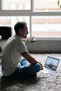 Man using laptop and having coffee while sitting on carpet