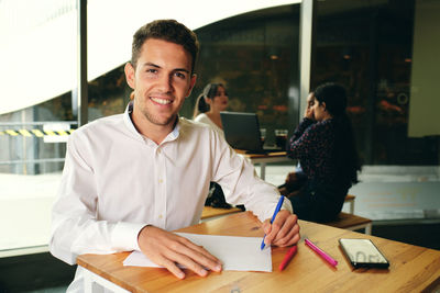 Portrait of smiling young man using smart phone on table