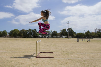 Side view of female athlete jumping over hurdle on field