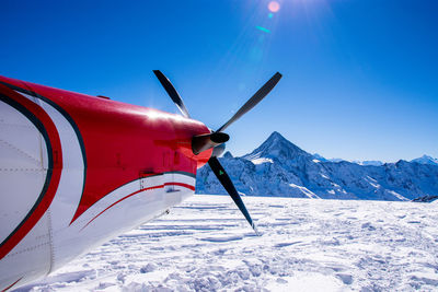 Airplane wing on snowcapped mountain against blue sky