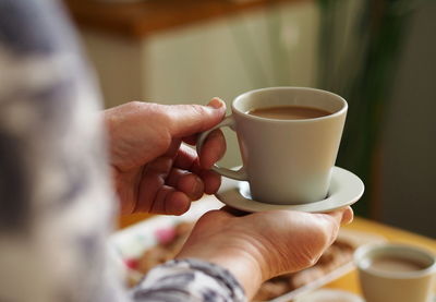 Elderly woman is hands hold a cup of coffee on the background of the kitchen. morning breakfast 
