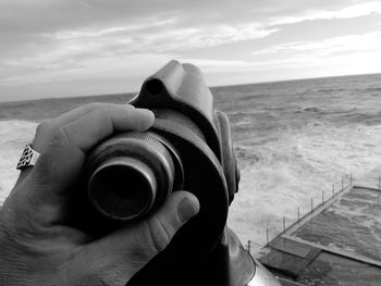 Cropped hand holding coin-operated binoculars against sky