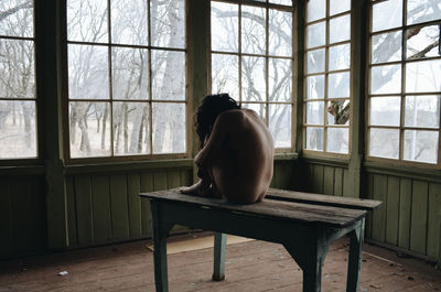 Full length of depressed naked woman sitting on table at home