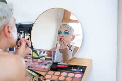 Young transgender looking at mirror and applying lipstick at dressing table