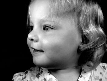 Close-up portrait of cute girl looking away against black background