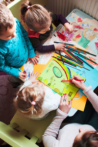 High angle view of mother and children painting on paper at home
