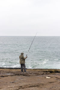 Rear view of man fishing on sea against sky