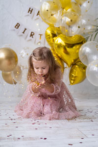 Happy child girl with long hair in pink dress blowing confetti and celebrating her birthday