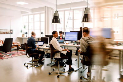 Male and female coworkers discussing while sitting at desk in office