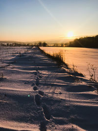 Scenic view of frozen field against sky during sunset